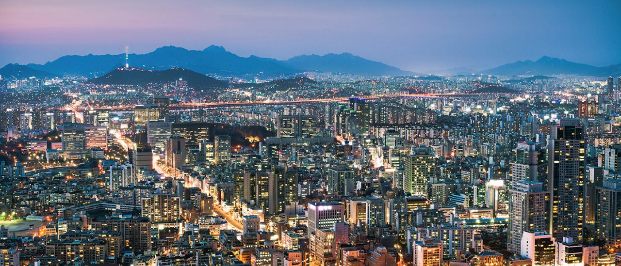 A view over South Korea's capital city, with the circular Seoul Arts Centre visible in the foreground, and N Seoul Tower on Namsan Mountain in the distance.